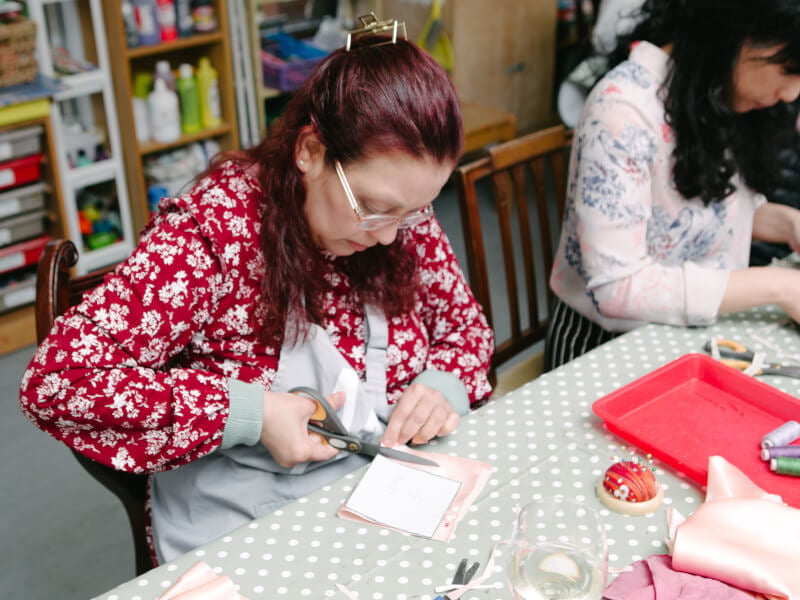 A person sits at a table, cutting round a paper pattern pinned to fabric