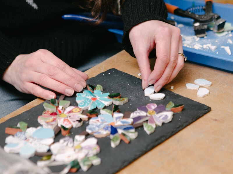 A close up of a person making a flower mosaic design using broken crockery pieces