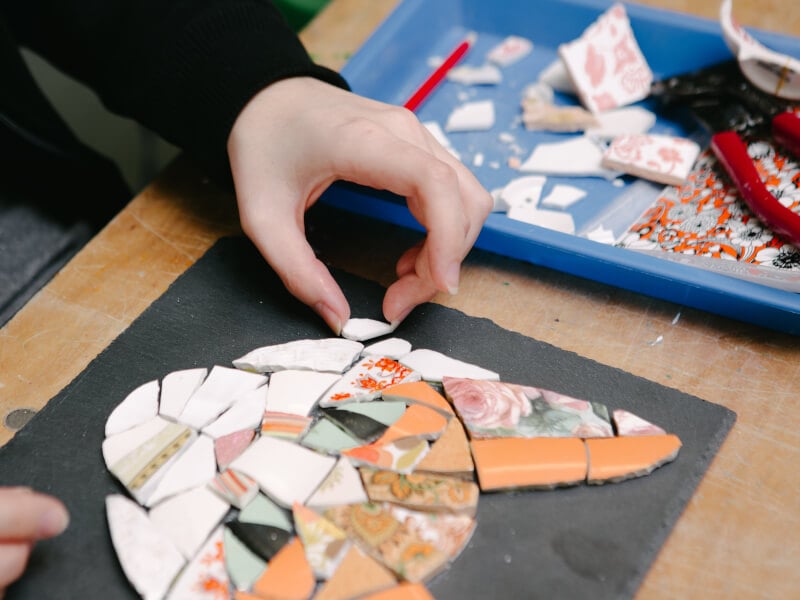 A close up of a hand arranging a piece of tile on a mosaic design of a cat