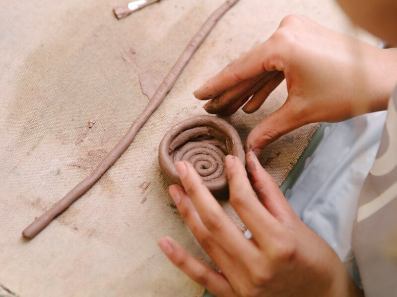 A close up of two hands making a coil pot at a pottery class