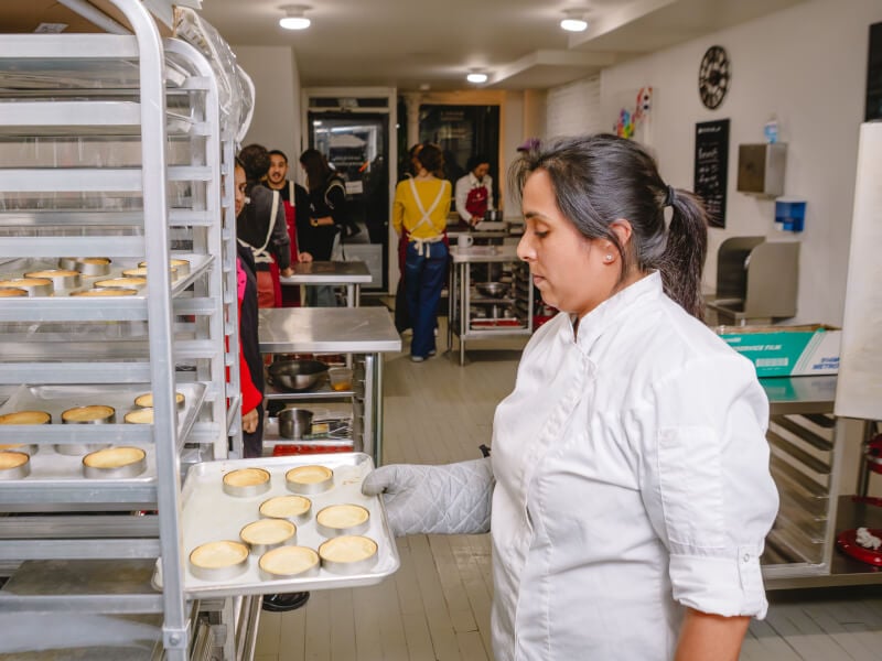 A baker taking a tray of pastry cases from a proving rack