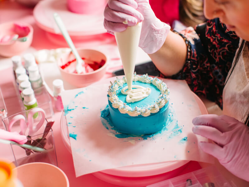 A close up of a person decorating a blue cake with white frosting