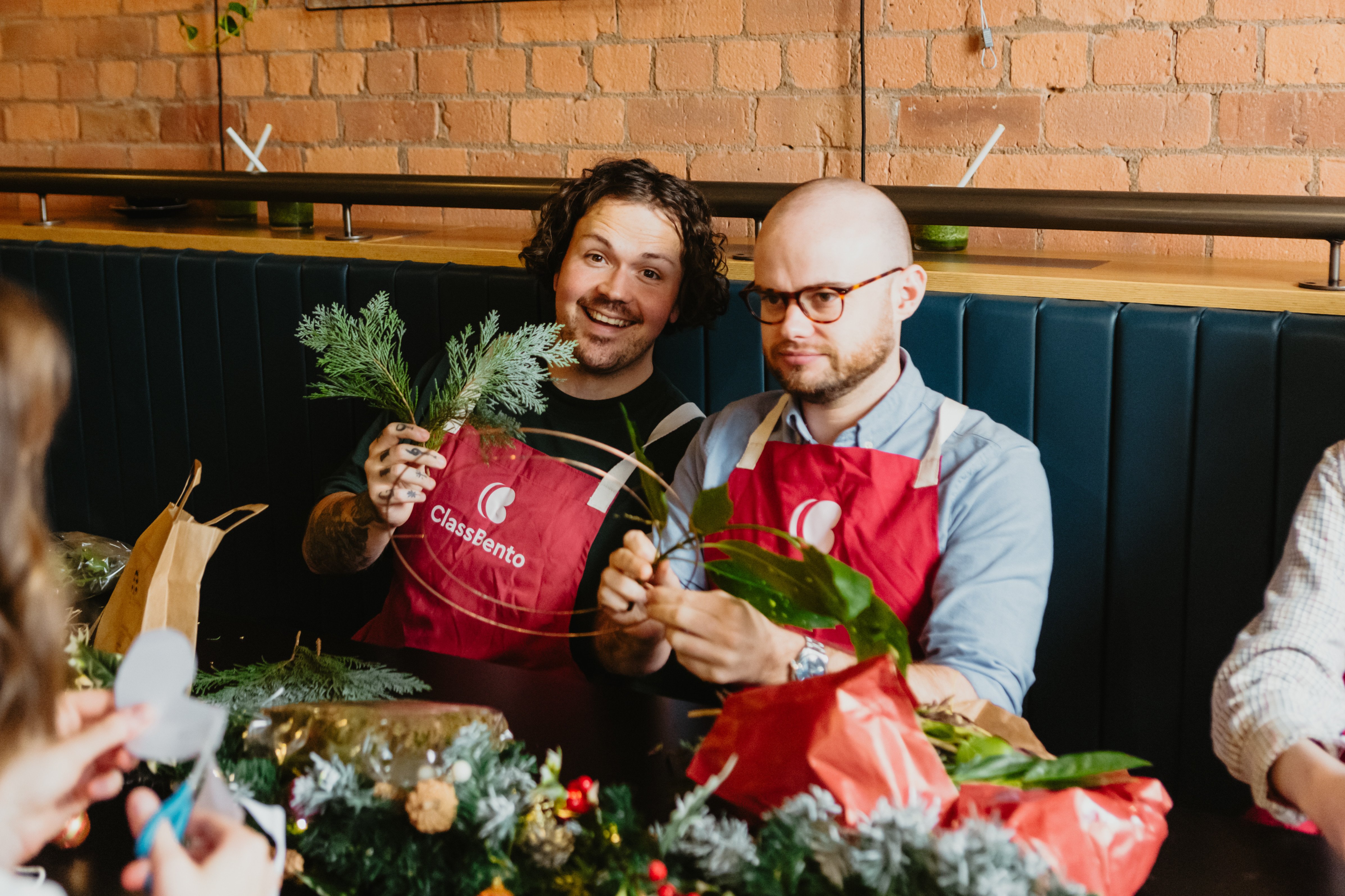 Two men smiling and laughing at a flower wreath arranging class