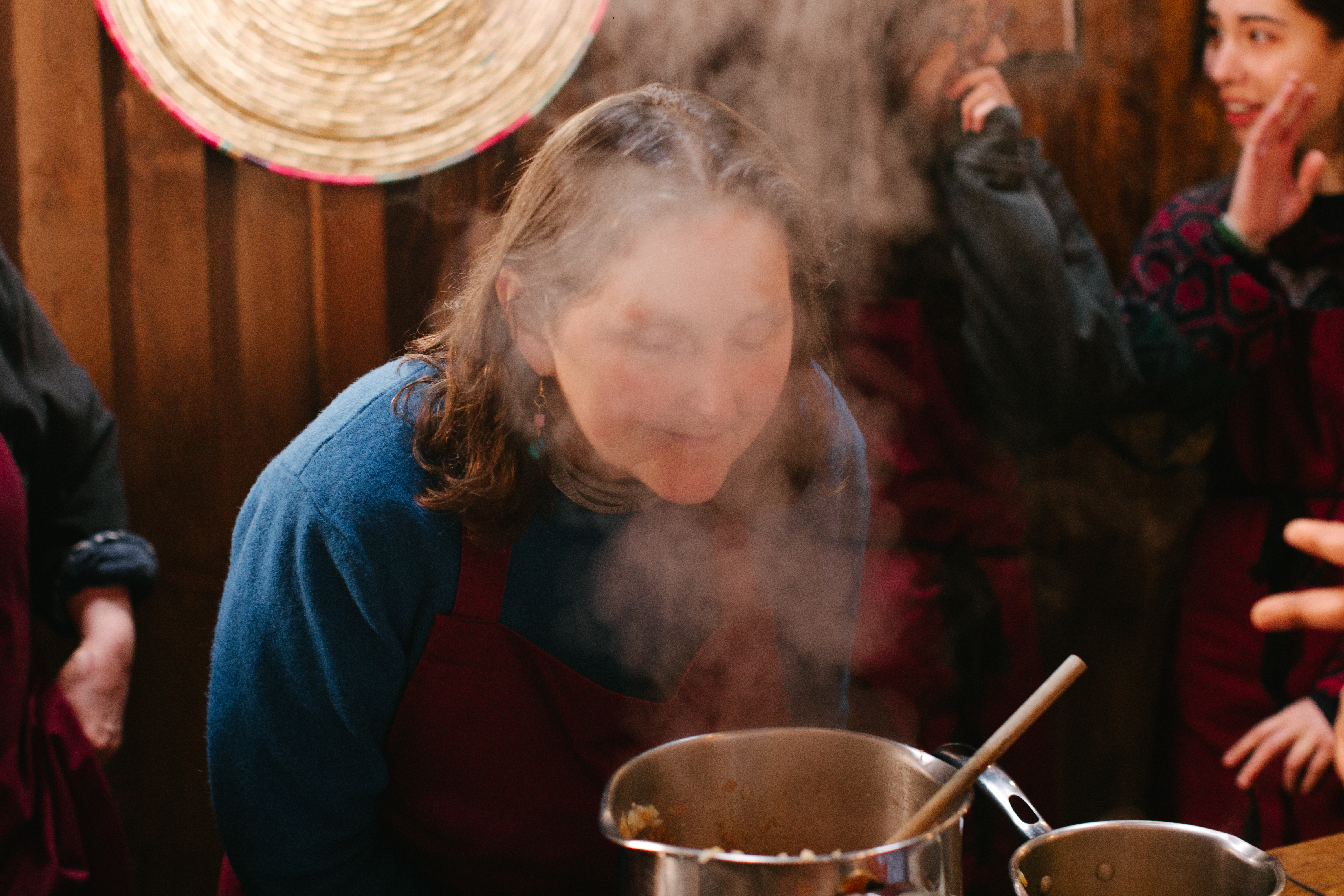 A woman smelling a pot on the stove immersed in stead at a mothers day cooking class 