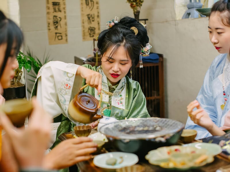 Three women in traditional Chinese dress at a tea tasting ceremony
