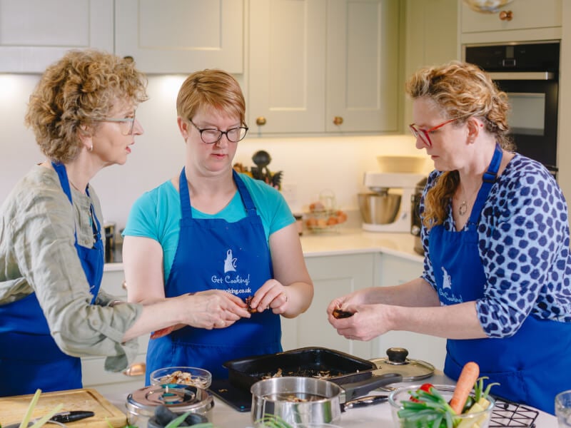 Three women at a cooking class wearing blue aprons