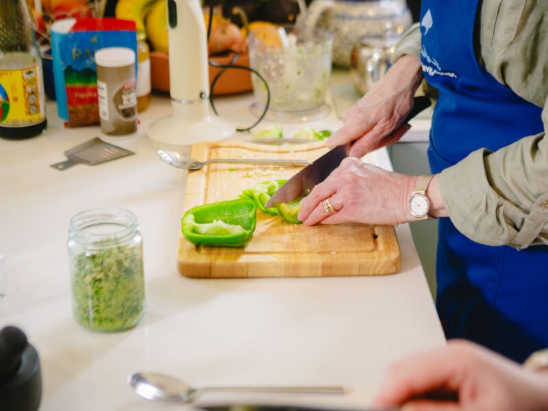 Close up of hands chopping a green bell pepper on a wooden chopping board