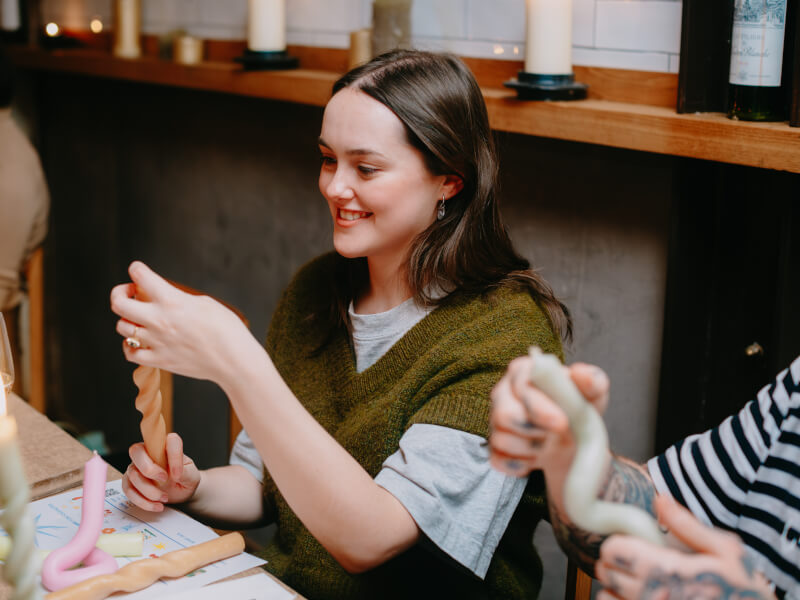 A woman is sitting at a table making bendy candles