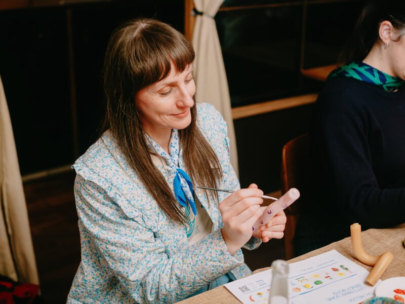 A woman in a blue flowery jacket is painting moon motifs on a pink candle