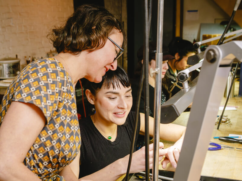 A teacher helping a student at a jewellery making class