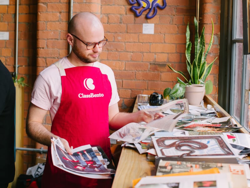 A man in an apron selecting papers for a collage class
