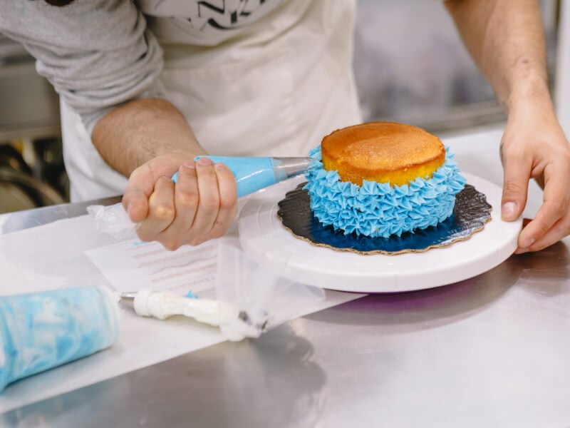 Close up of a person piping blue frosting onto a cake