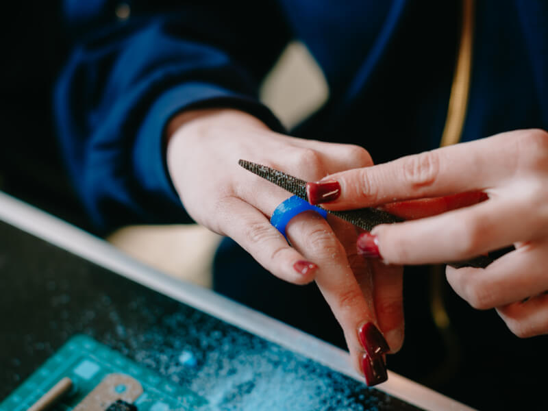 A person is filing a blue wax ring mould that they've placed on their finger