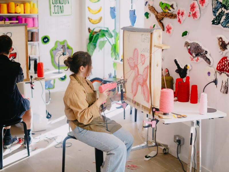 A rug tufting workshop focusing on a woman making a rug design of a pink balloon animal