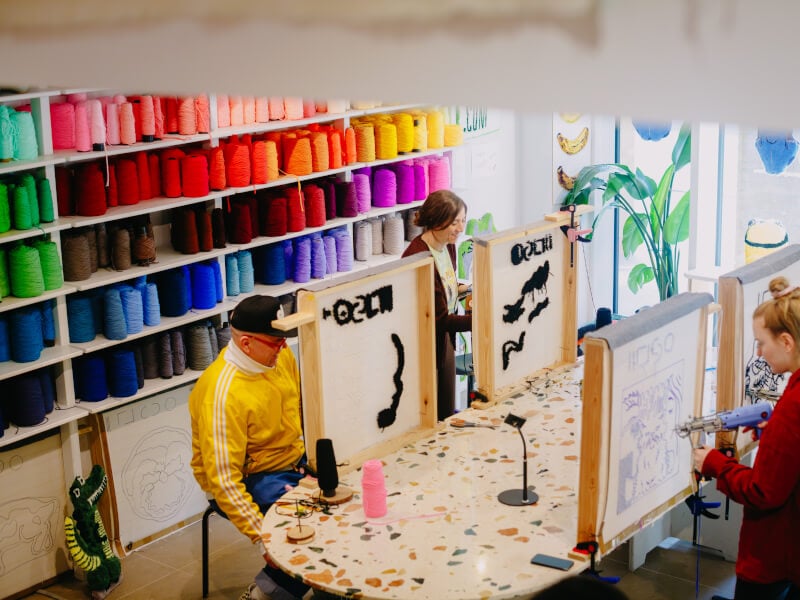 A shot from above of a tufting studio, featuring four students at canvases, making handmade rugs