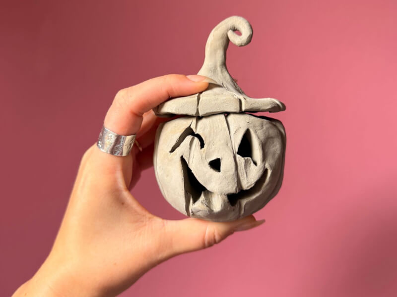 A person holding up a clay sculpted pumpkin