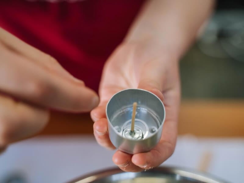Close up on a hand holding a metal tealight container and wick up to the camera