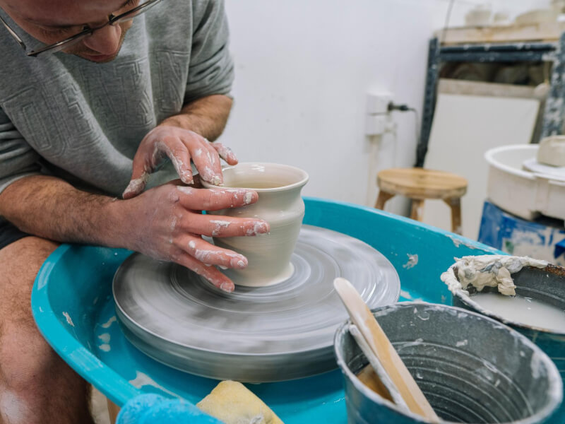 Person leaning forward making pottery during wheel throwing class. 