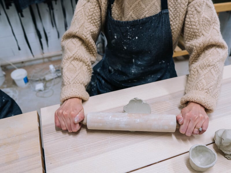 A person in a cream sweater rolling out clay to be used in sculpting