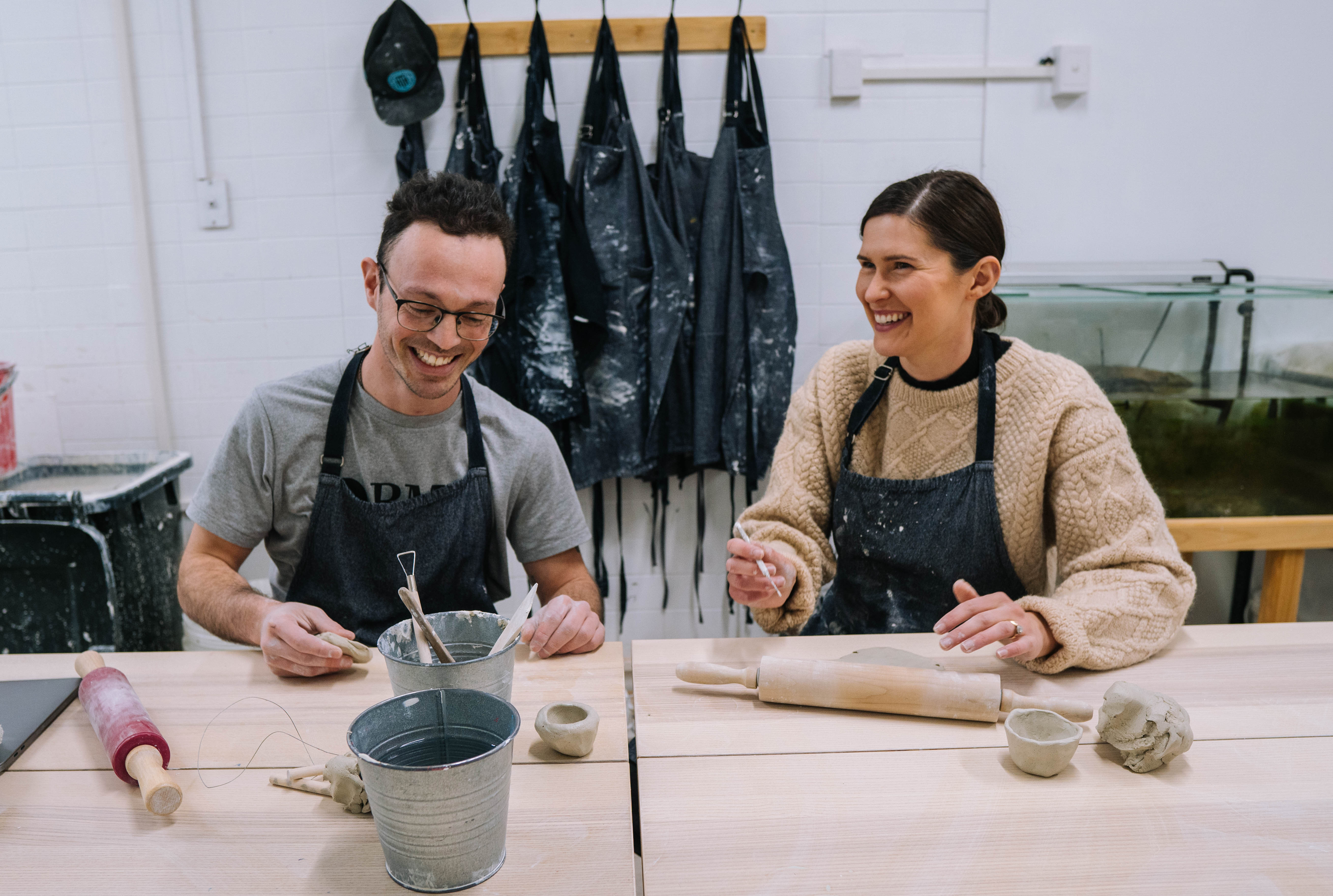 Two people sitting side by side, smiling and laughing as they make pottery together