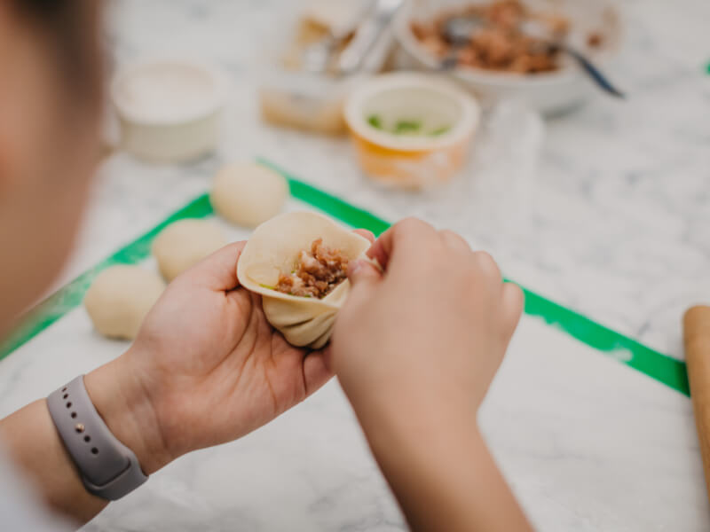 A close up of a person filling an Chinese dumpling before cooking
