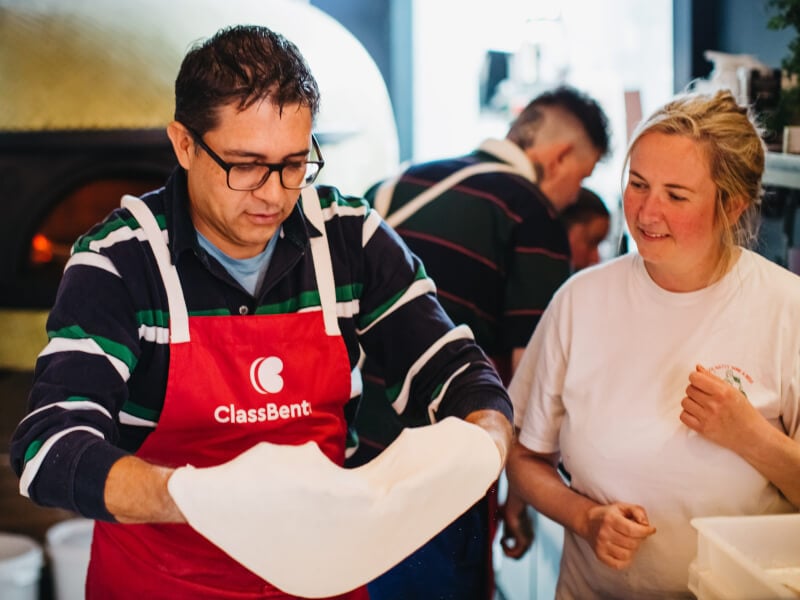 A man is stretching dough between is hands in a pizza making class.