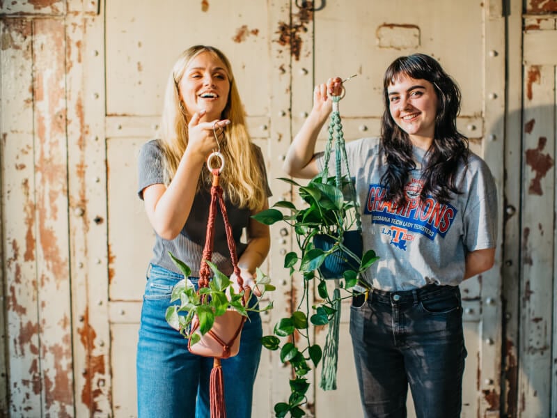 Two women hold up their DIY macramé plant hangers.