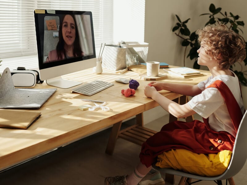 a child works with modeling clay with a teacher over a virtual craft class