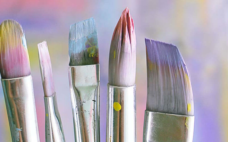 Five paintbrushes covered in colourful paint