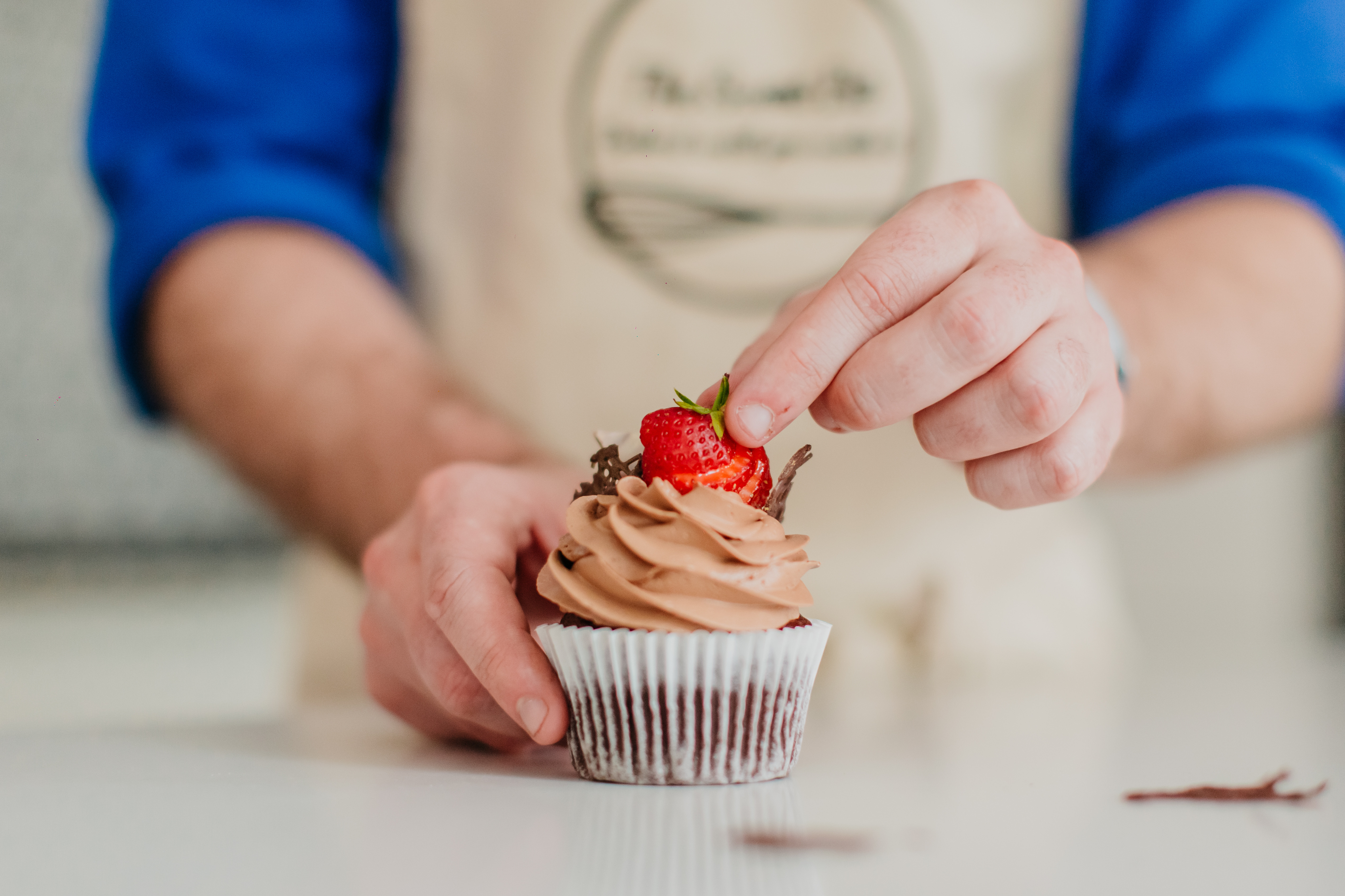 Close up of hands topping a chocolate cupcake with sliced strawberries