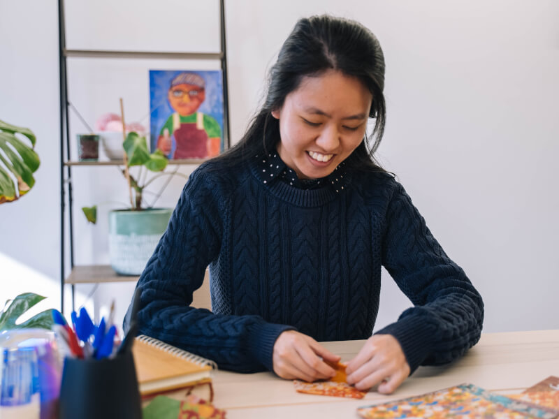 A woman smiling while practising origami on a white table