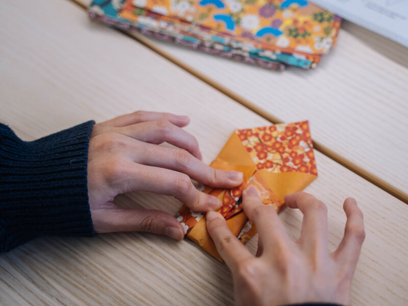 Close up of hands pressing down on orange patterned craft paper to create paper folds