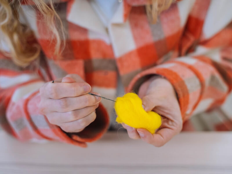 Close up of hands crafting a needle felted item with yellow wool