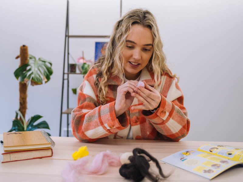 Woman smiling whilst needle felting with brightly coloured yarns at a sewing and embroidery class