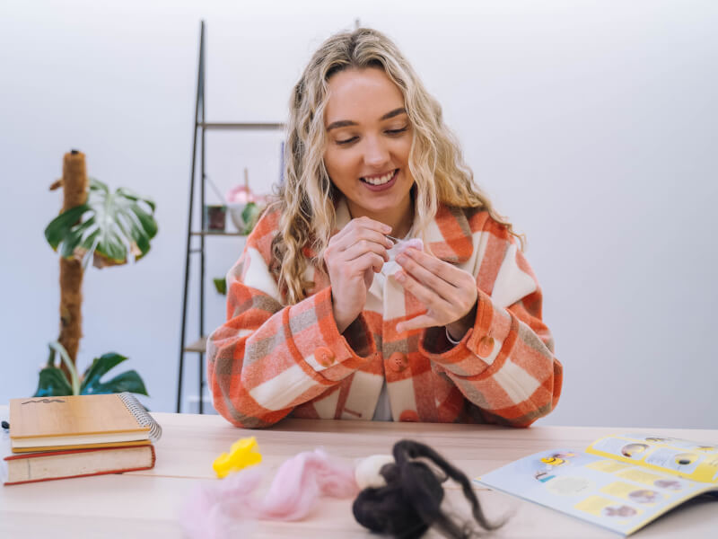 Smiling woman in a checked jacket needle felting with yellow wool