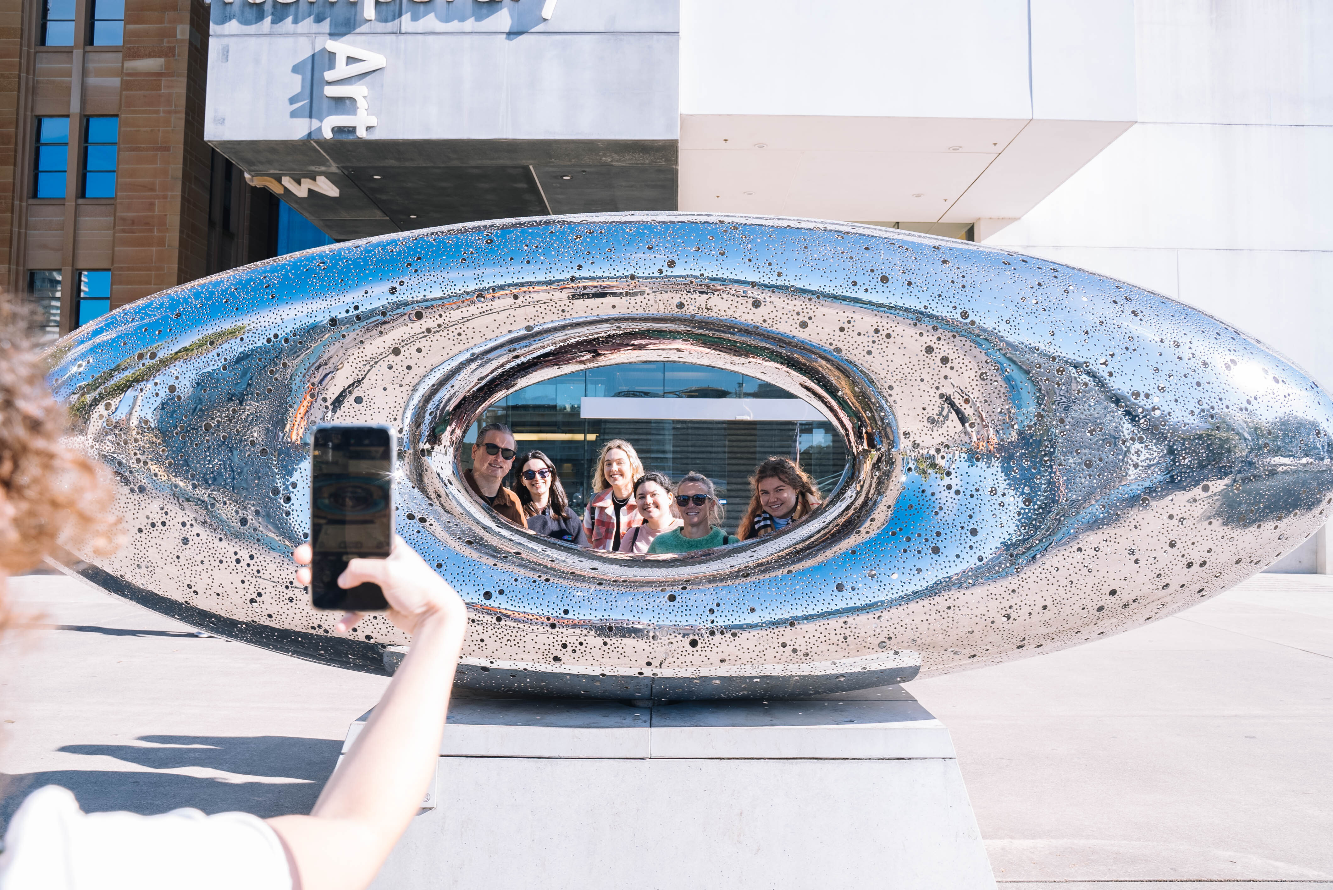 Someone taking a photo of a silver metallic sculpture of an eye