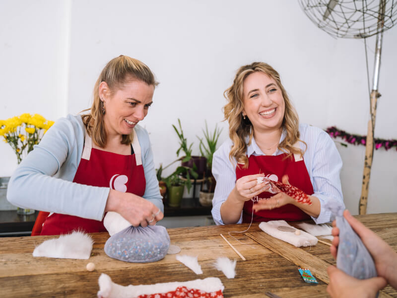 Two women in aprons smiling at a sewing class