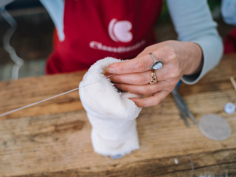 A woman's hand sewing a white fluffy piece of fabric with white thread
