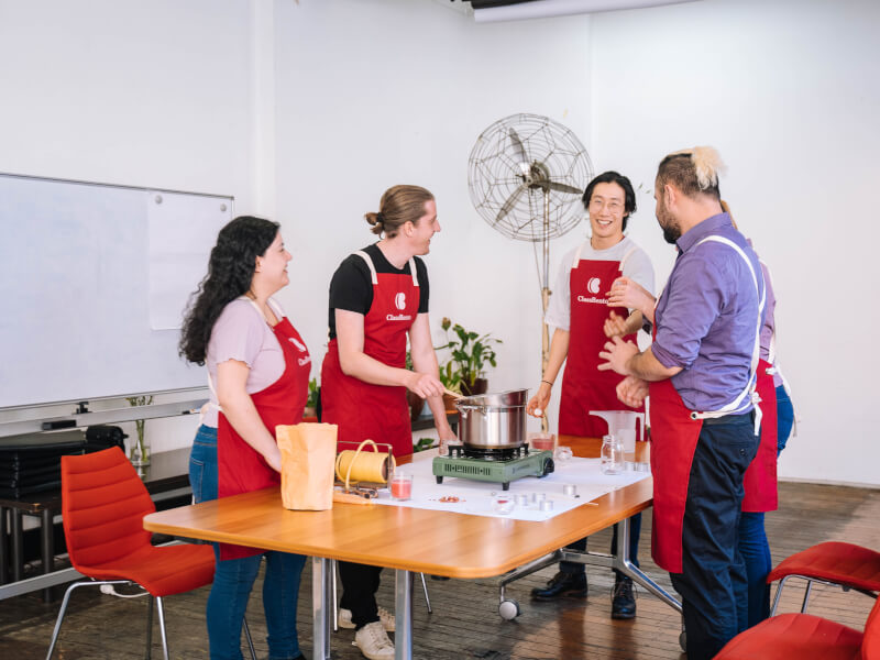 Four people at a candle making class, smiling and laughing as they listen to the teacher