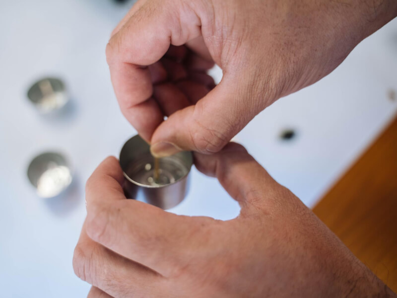 A pair of hands setting a wick in a metal tealight housing