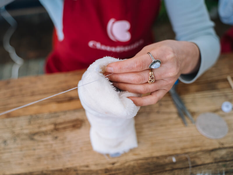 Hands sewing with white thread and needle.