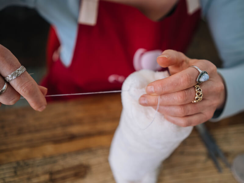 Hands wearing rings holding white thread. 