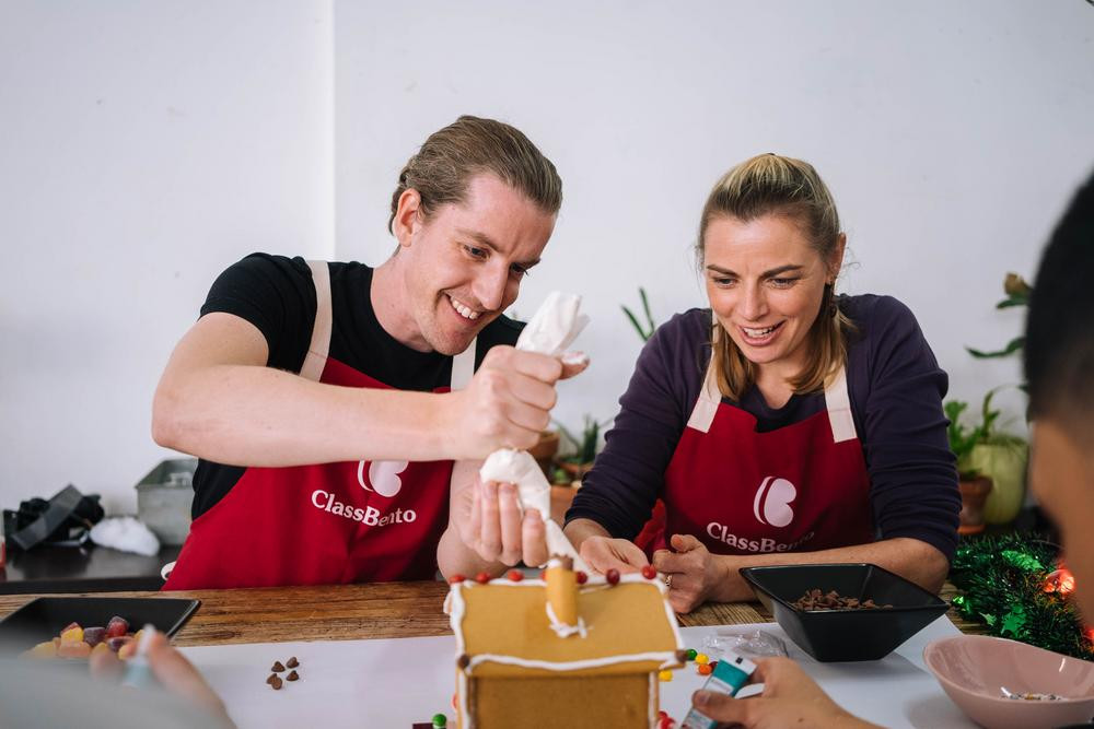 A couple piping icing onto a gingerbread house together