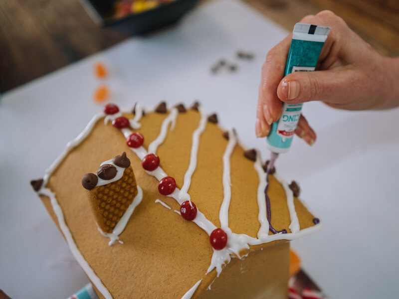 Top down shot of a gingerbread house being piped with purple and white icing