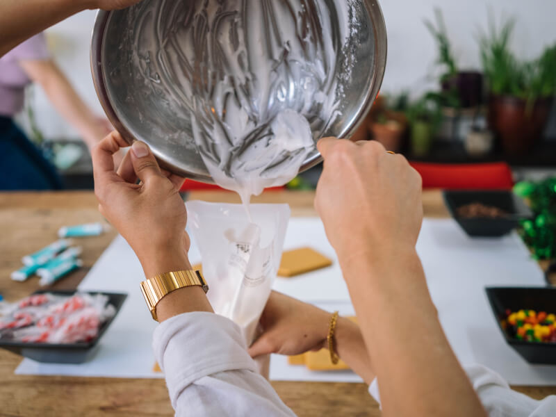 A bowl of icing being poured into an piping bag at a cake decorating class.