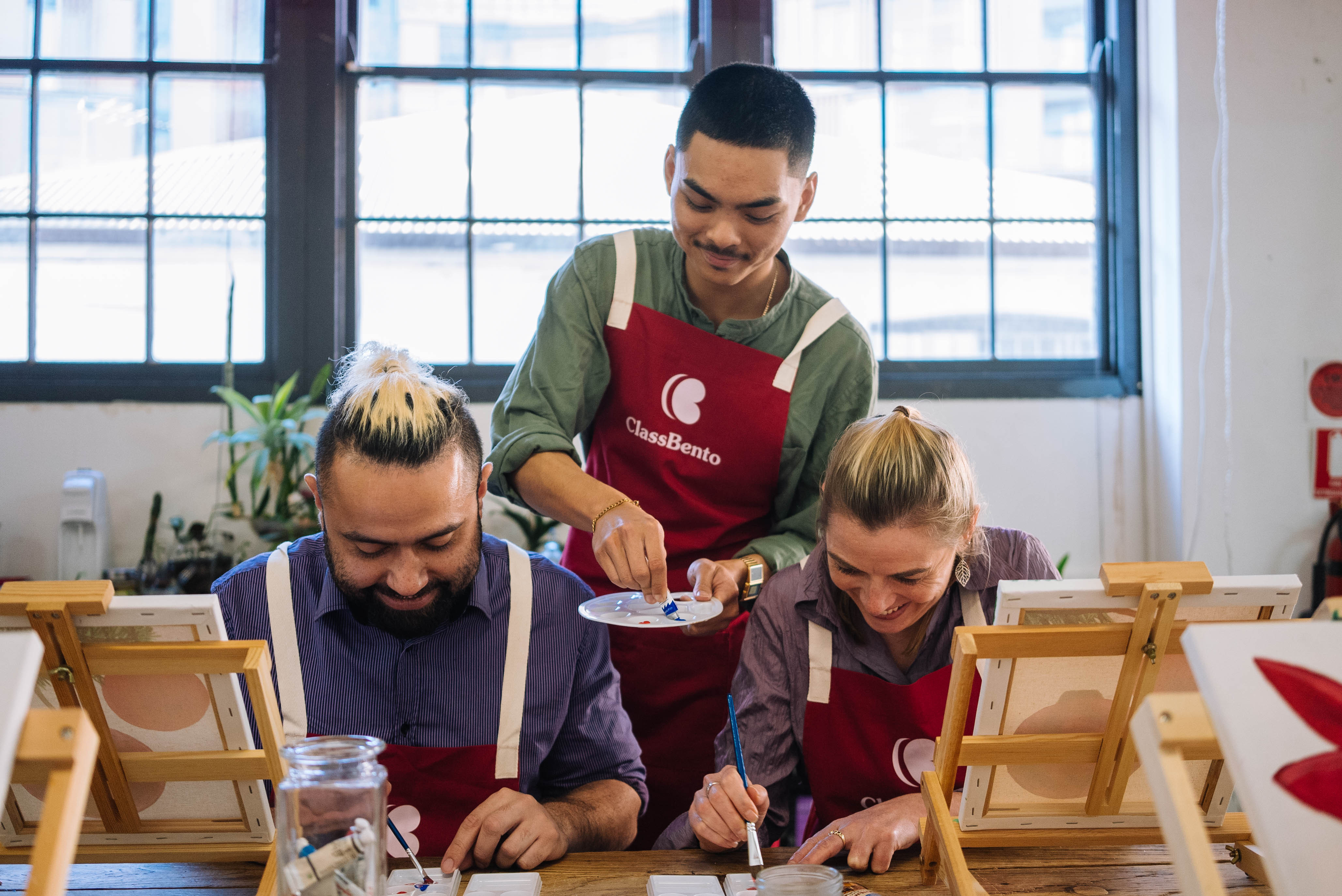 A teacher standing behind two students at a painting class