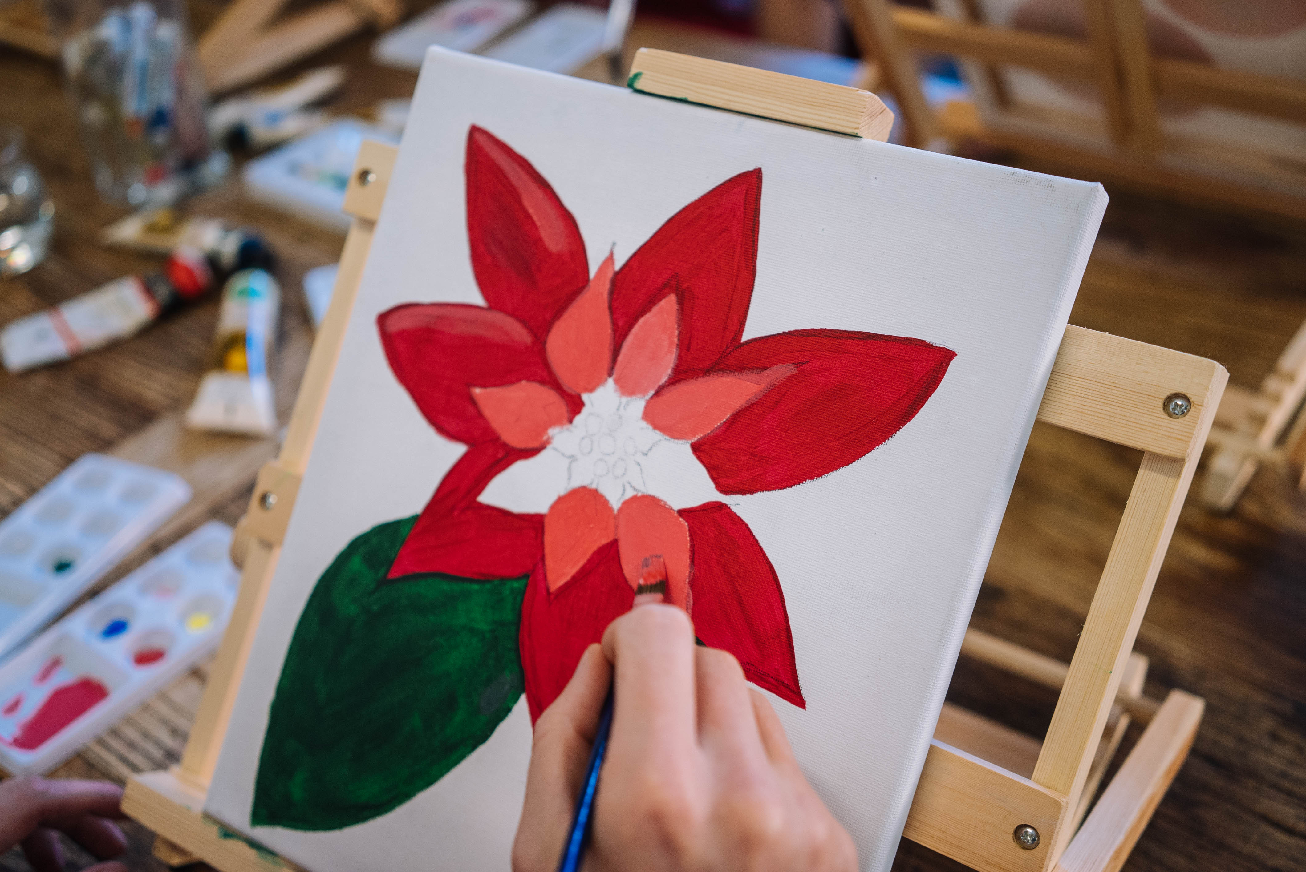 Close up of a person painting a Christmas-themed flower on canvas