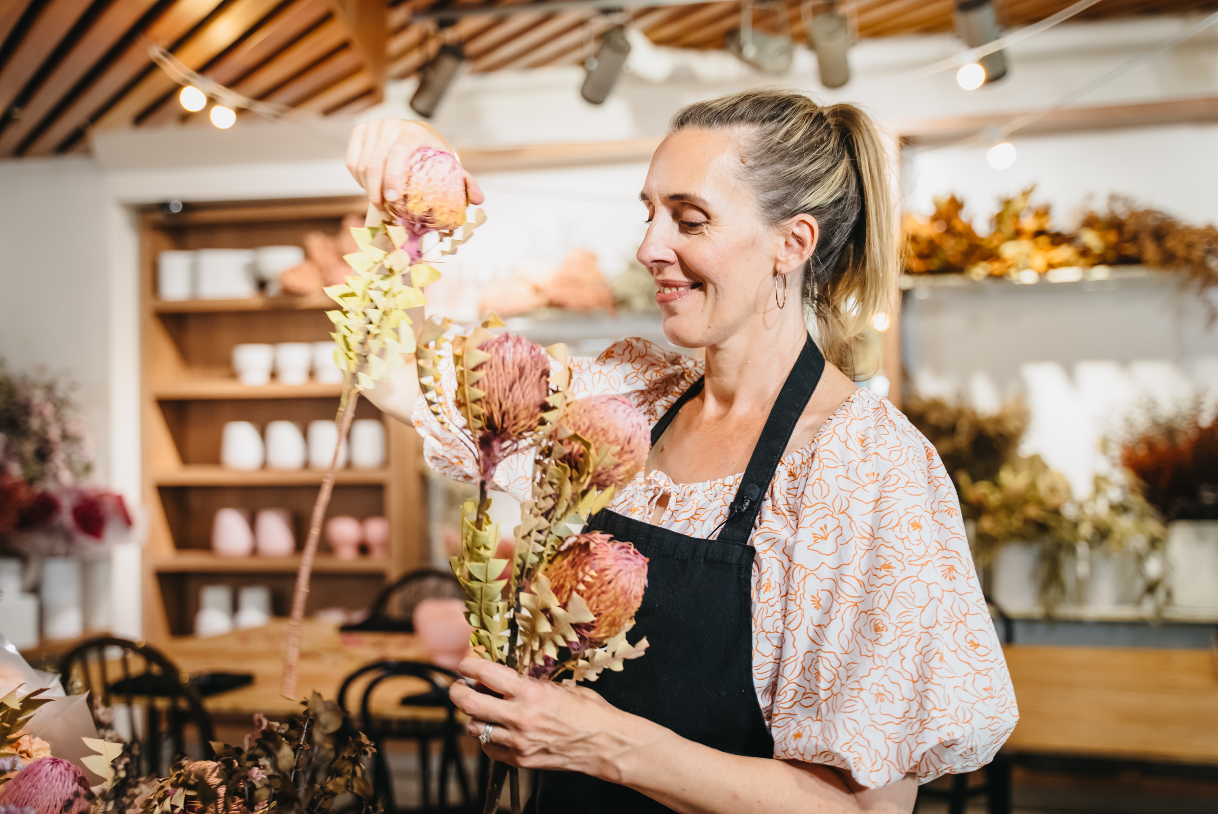 A smiling woman adding to the dried floral bouquet she's holding