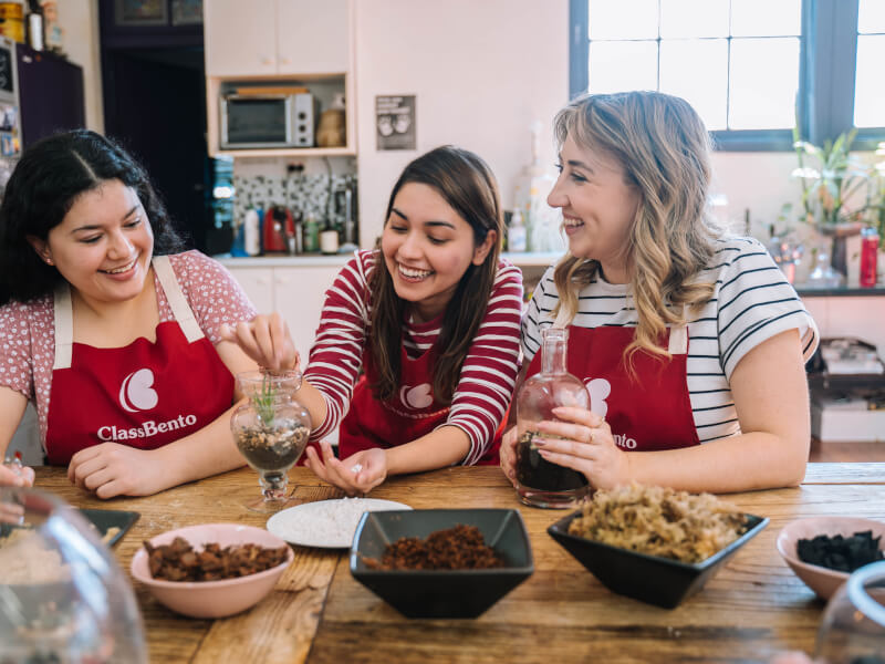 Three women wearing red aprons smiling at a team building class.