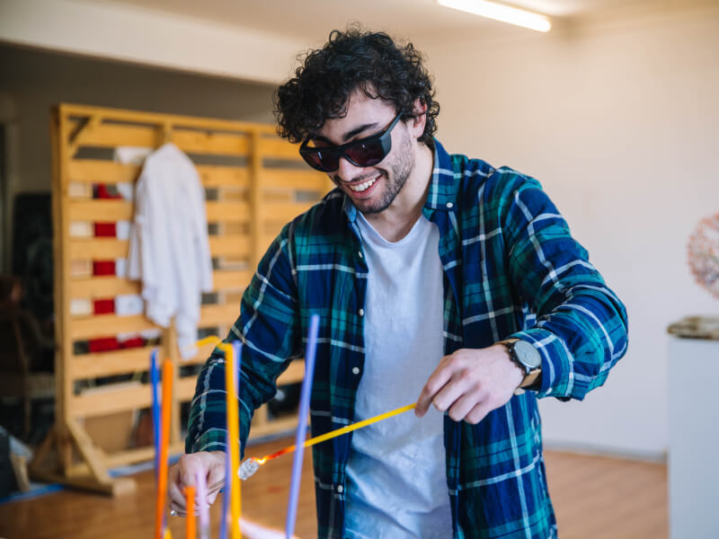 A man is smiling and shaping molten glass with a hot poker
